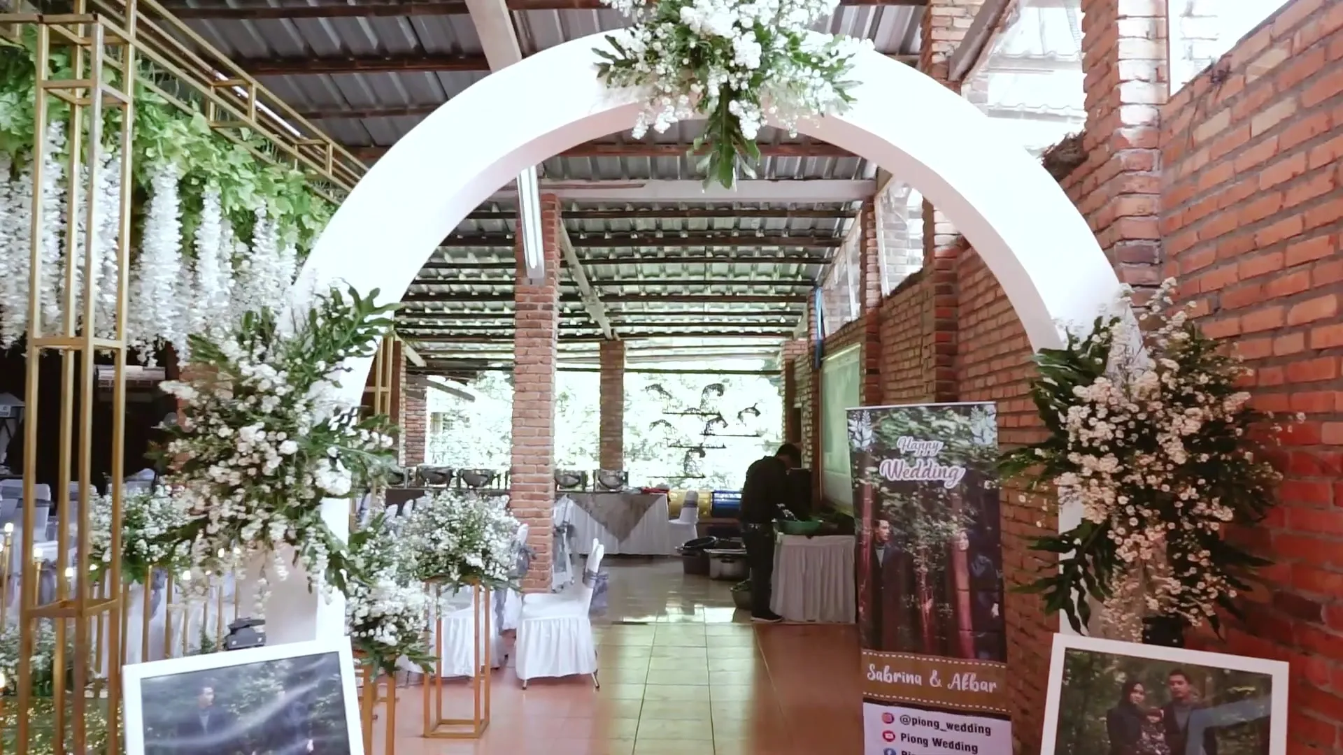 Gerbang lengkung putih berhias bunga di venue bata merah