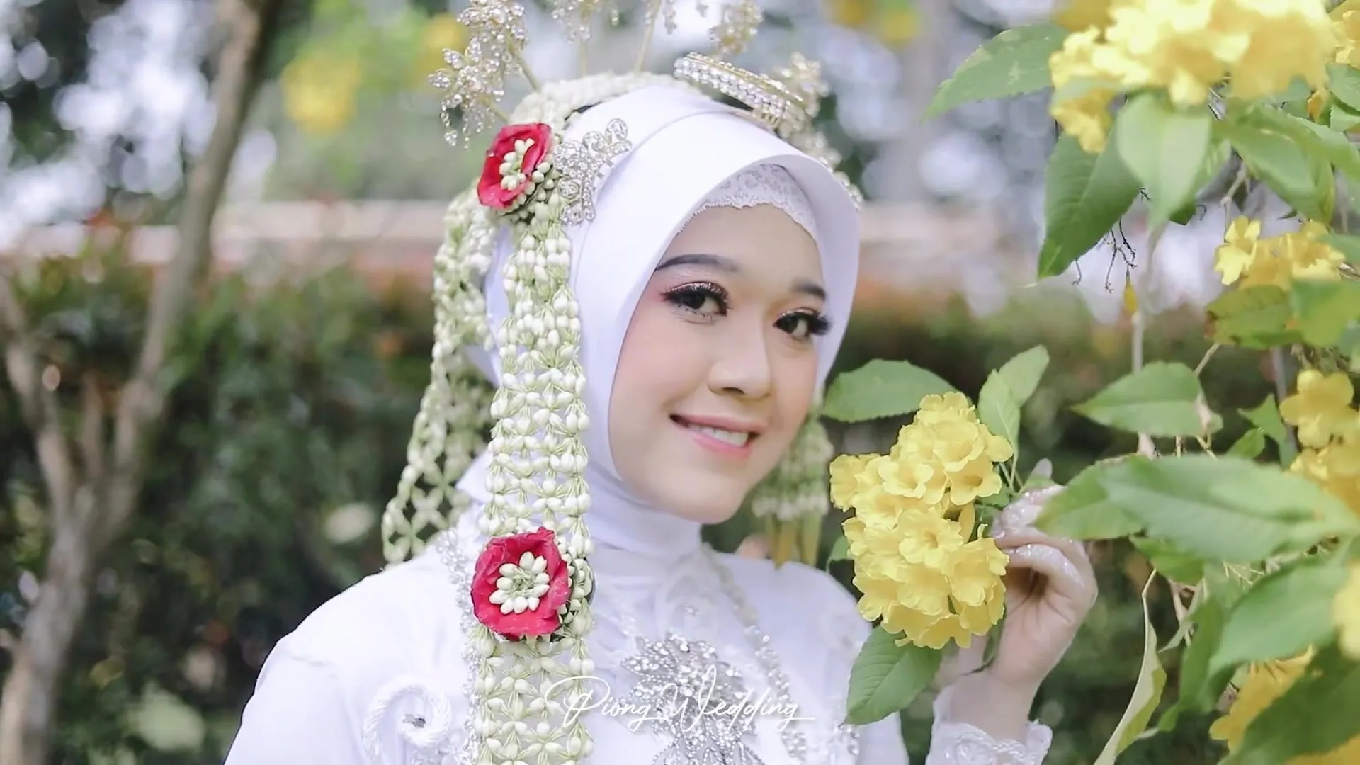 Pengantin perempuan berhijab putih tersenyum di antara bunga kuning